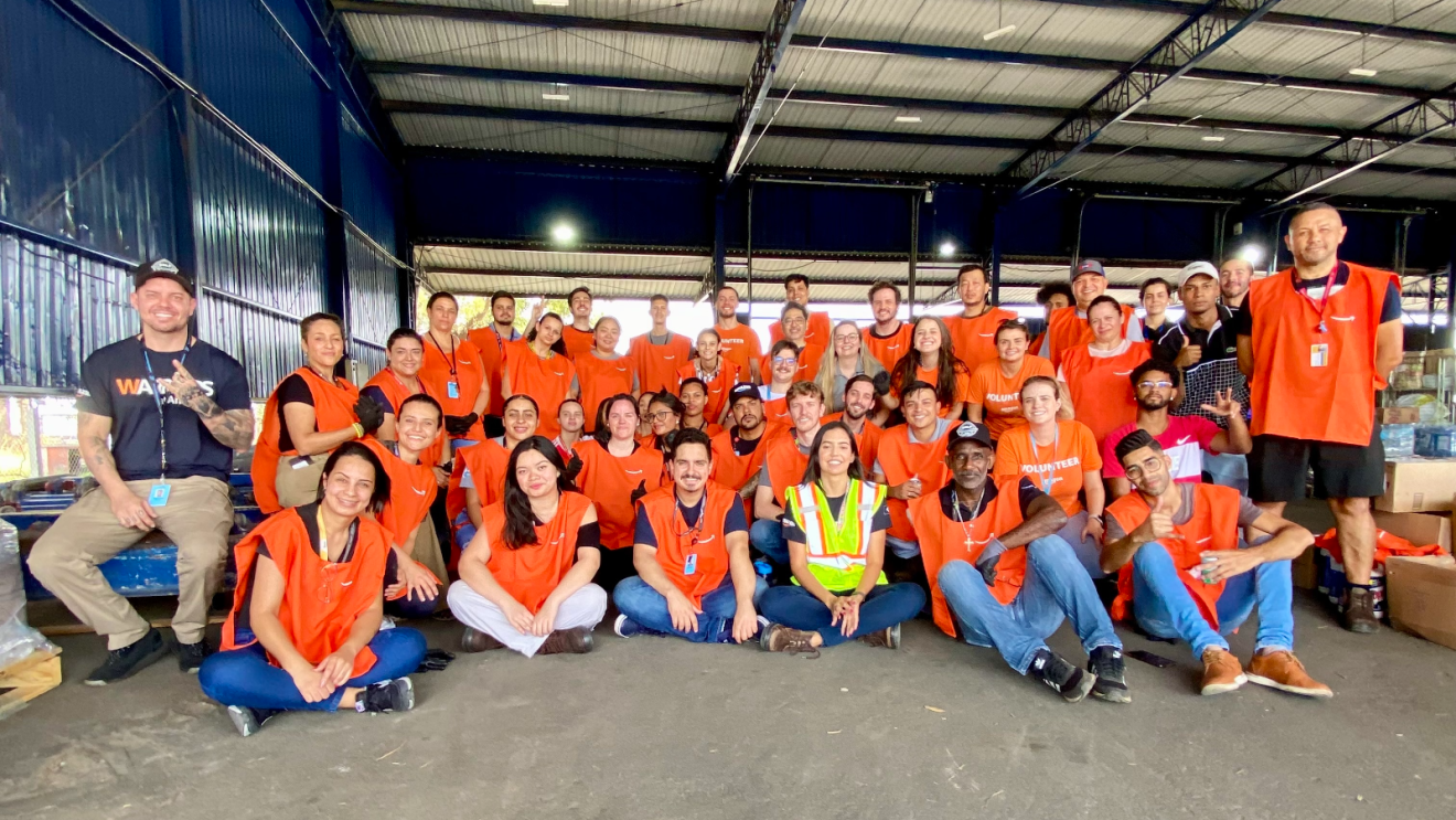 A group of Amazon volunteers wear matching orange "Amazon volunteer" vests smile for a group photo.