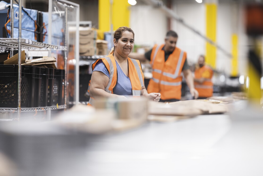 Amazon Mitarbeiterinnen und Mitarbeiter in einem Verteilzentrum bereiten die Päckchen für die Zustellung vor.