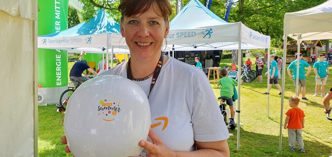 Eine lächelnde Frau im Amazon T-Shirt hält einen weißen Luftballon auf dem "I love summer" zu lesen ist