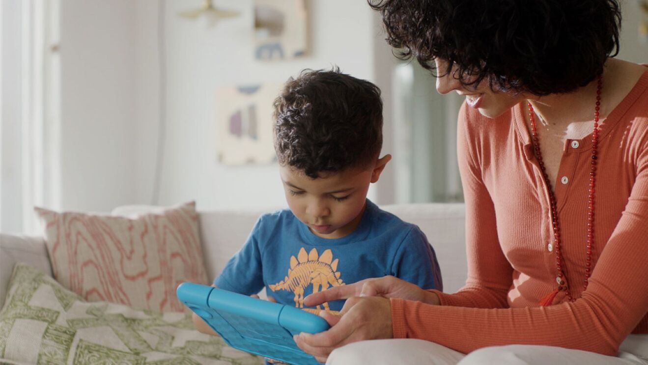 Mother and son view Amazon Fire tablet together on couch.