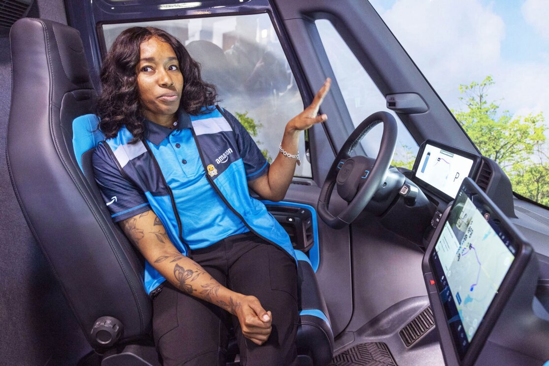 A photo of Brandi Monroe, a delivery driver for Kangaroo Direct, an Amazon Delivery Service Partner sitting in the driver seat of an Amazon delivery van from Rivian.