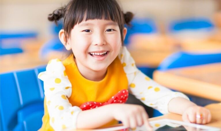 Smiling toddler girl sits at the desk with tablet.