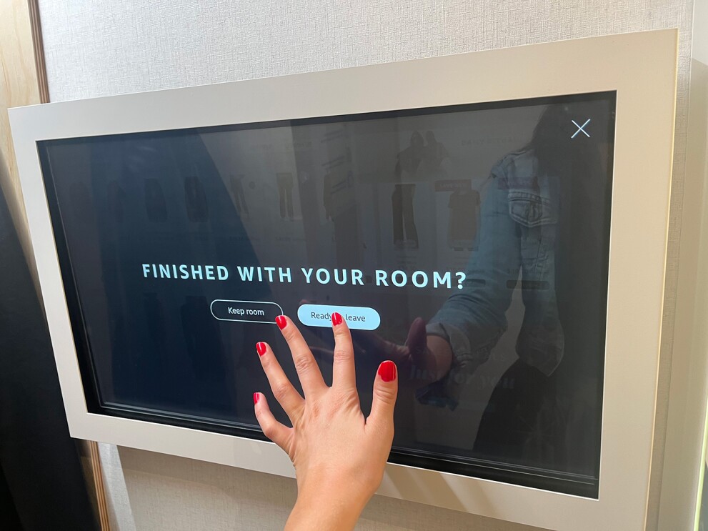 An image of a hand tapping the option to close the fitting room on a touch screen on the wall.