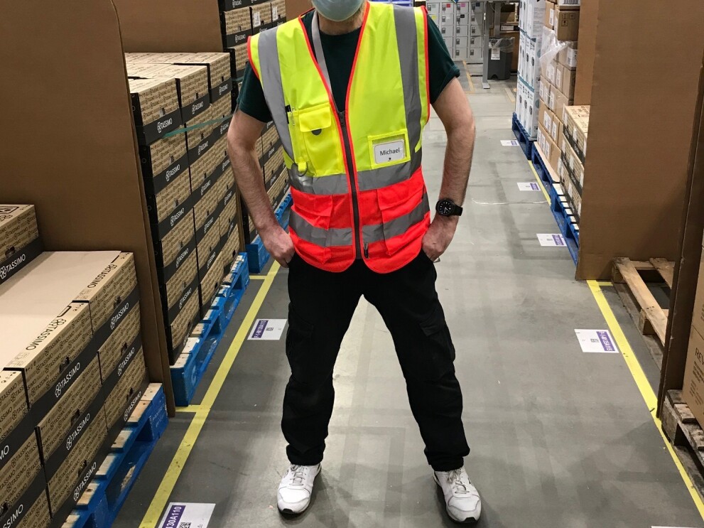 Michael Power, temp flow director, standing in the fulfilment centre while wearing a facemask and a hi-vis jacket.