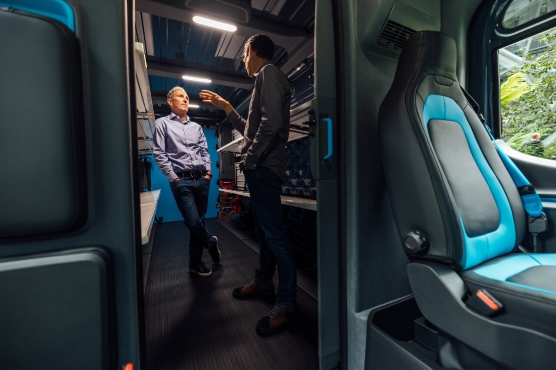 Andy Jassy and RJ Scaringe stand inside the back of Rivian Amazon delivery vehicle while chatting.