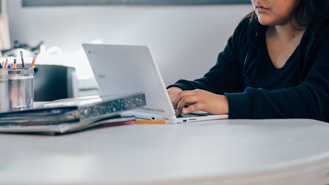 A student types on a laptop computer, while sitting at a table. 
