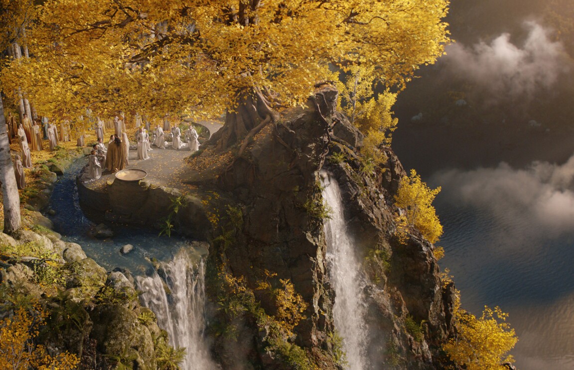 An image of a cliff with a waterfall on the ledge and a large body of water below. There are treed in the background and people gathered around the edge. It is a scene from Amazon's The Lord of the Rings: The Rings of Power series.