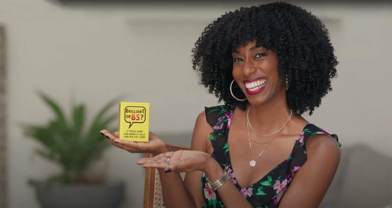 A woman holds a box while smiling. The box of cards reads "Brilliant or BS"