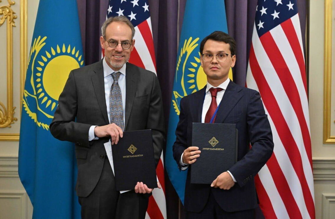 Two officials holding documents in front of US and Kazakhstan flags