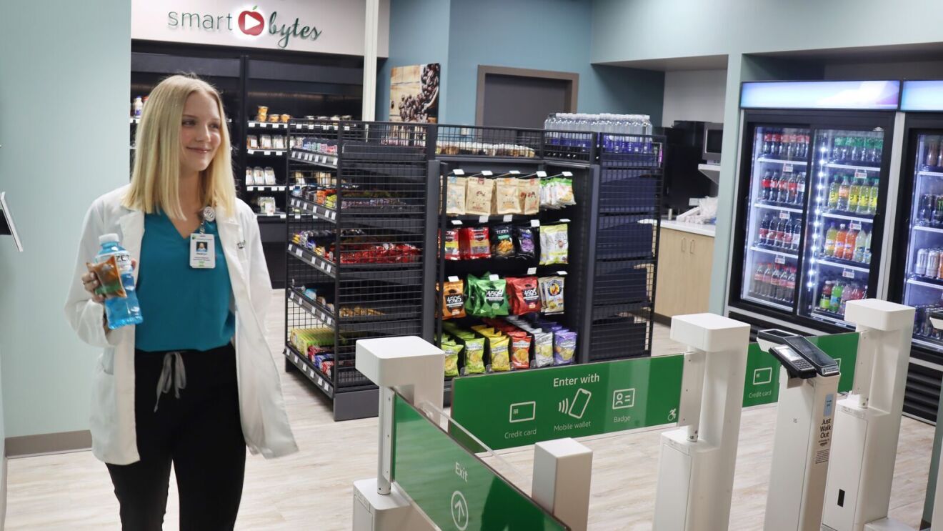 A photo of a hospital employee leaving a hospital retail store's gates powered by Just Walk Out technology, holding a beverage and a snack.