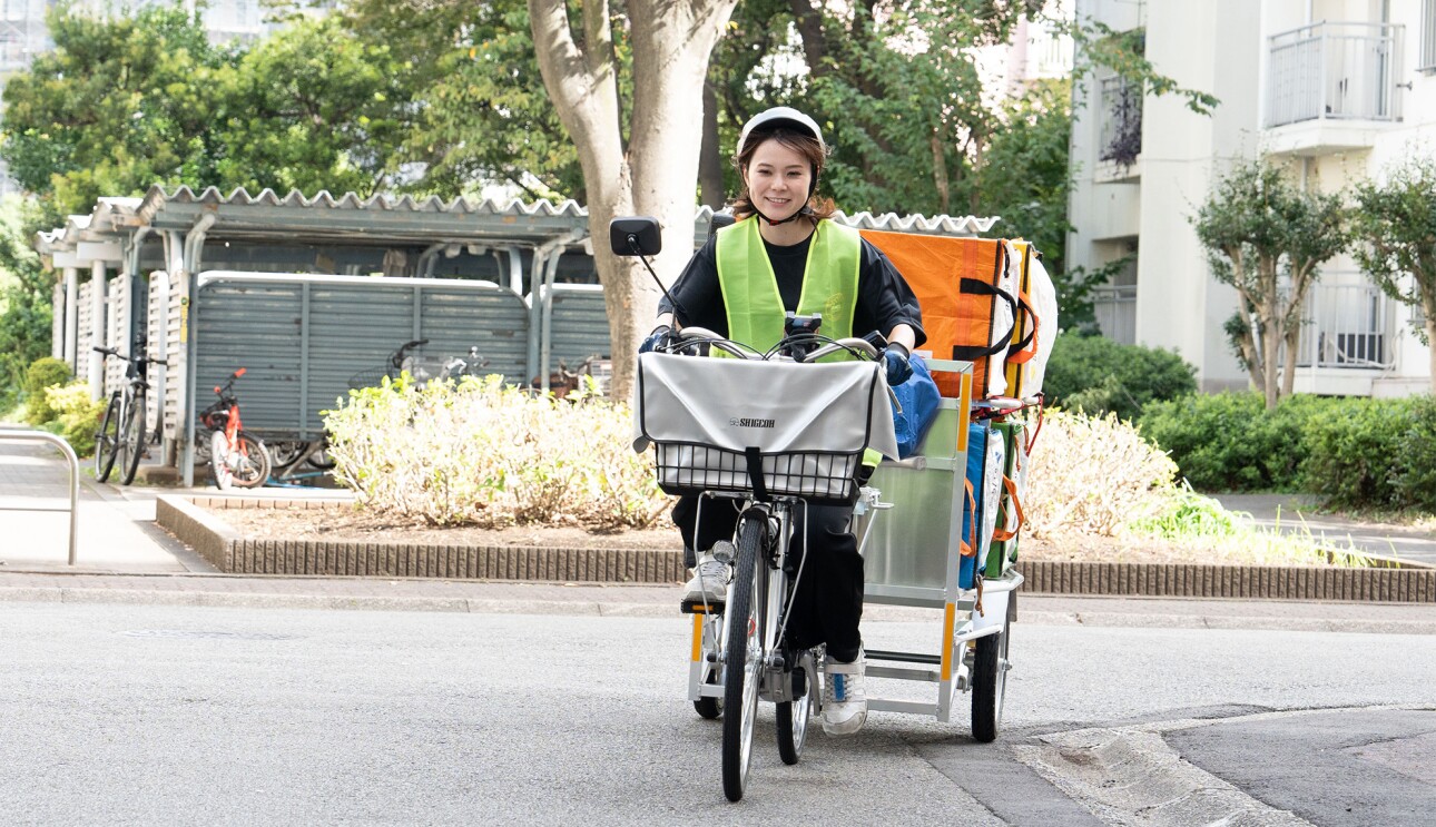 団地の敷地内を荷台が付いた電動アシスト付き自転車で走る女性