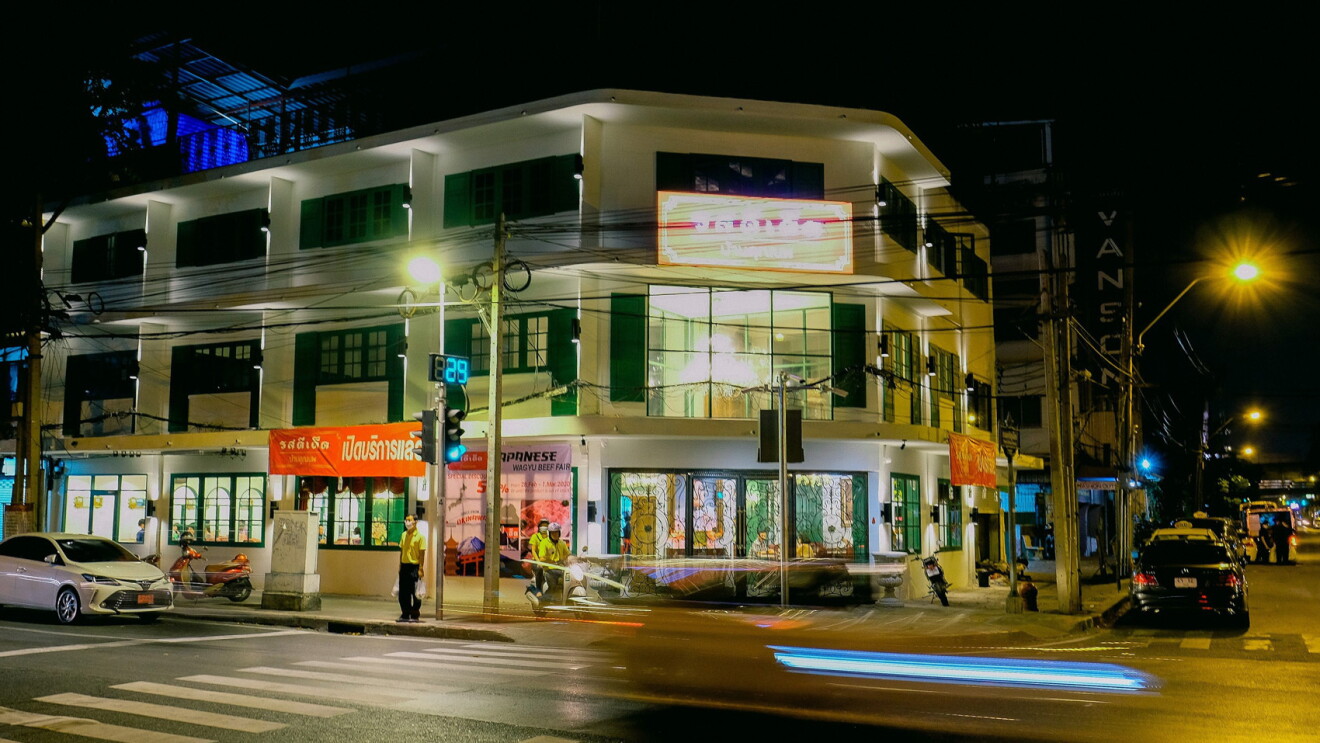 An image of a building with shops on the corner of a street in a city in Thailand.