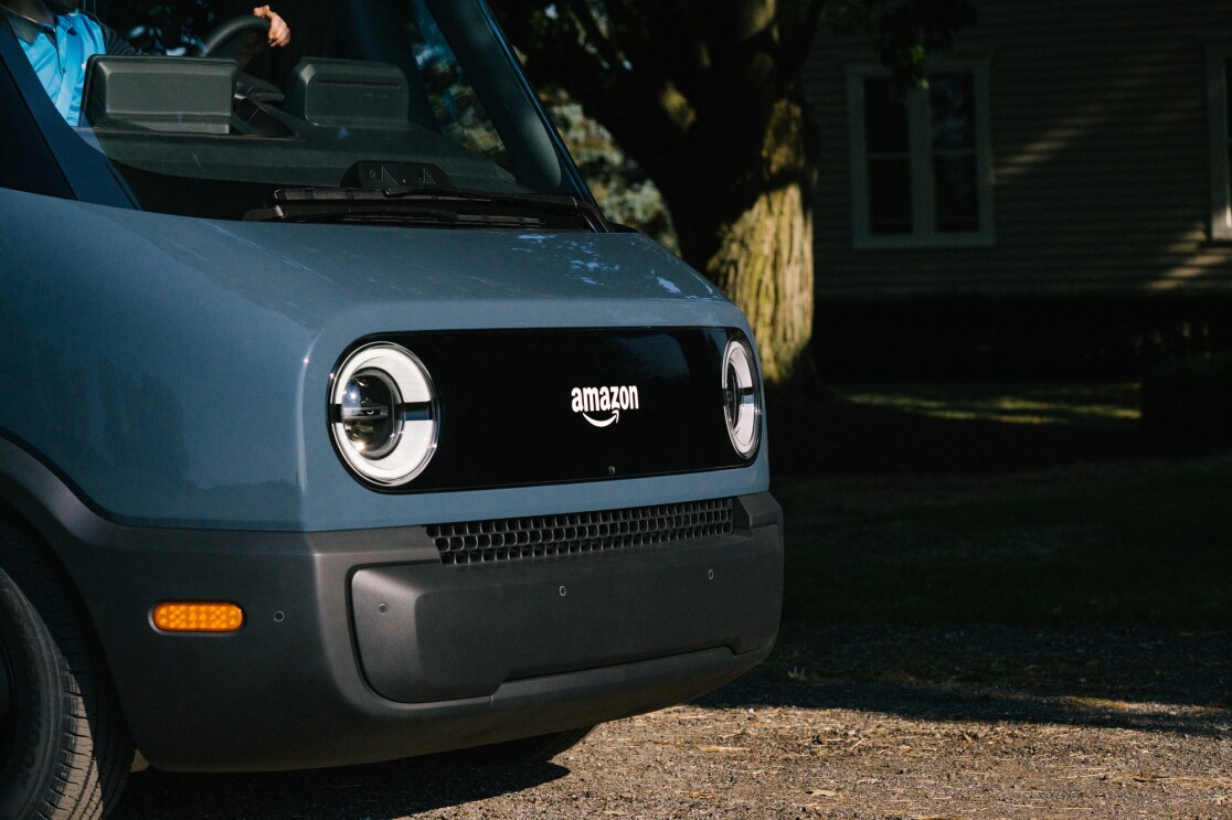 The front end of an electric delivery vehicle, showing headlights and the Amazon logo.