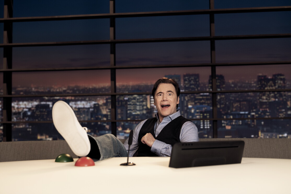 Michael „Bully“ Herbig mit hochgeschlagenen Beinen hinter einem Schreibtisch. Mit LOL – „Last One Laughing“ präsentiert er die erste deutsche Comedy-Gameshow bei Amazon Prime.