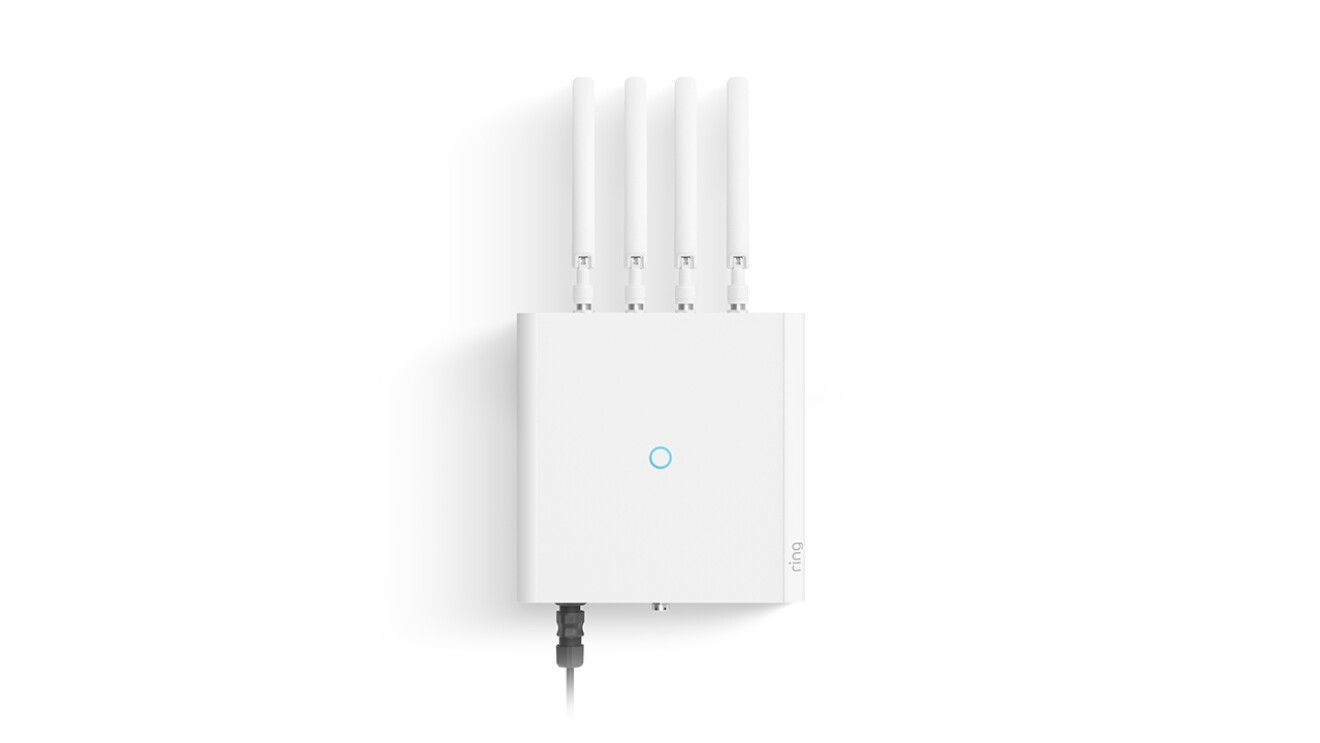 An image of a white device with several white, metal prongs coming out of it. In the center of the device is a blue ring symbol, and the side of the device has the gray Ring logo on it.