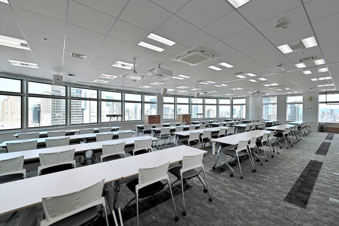 会議室では窓が広がっている。その会議室に数台のロングテーブルと椅子、表彰台が置かれて並んでいる。