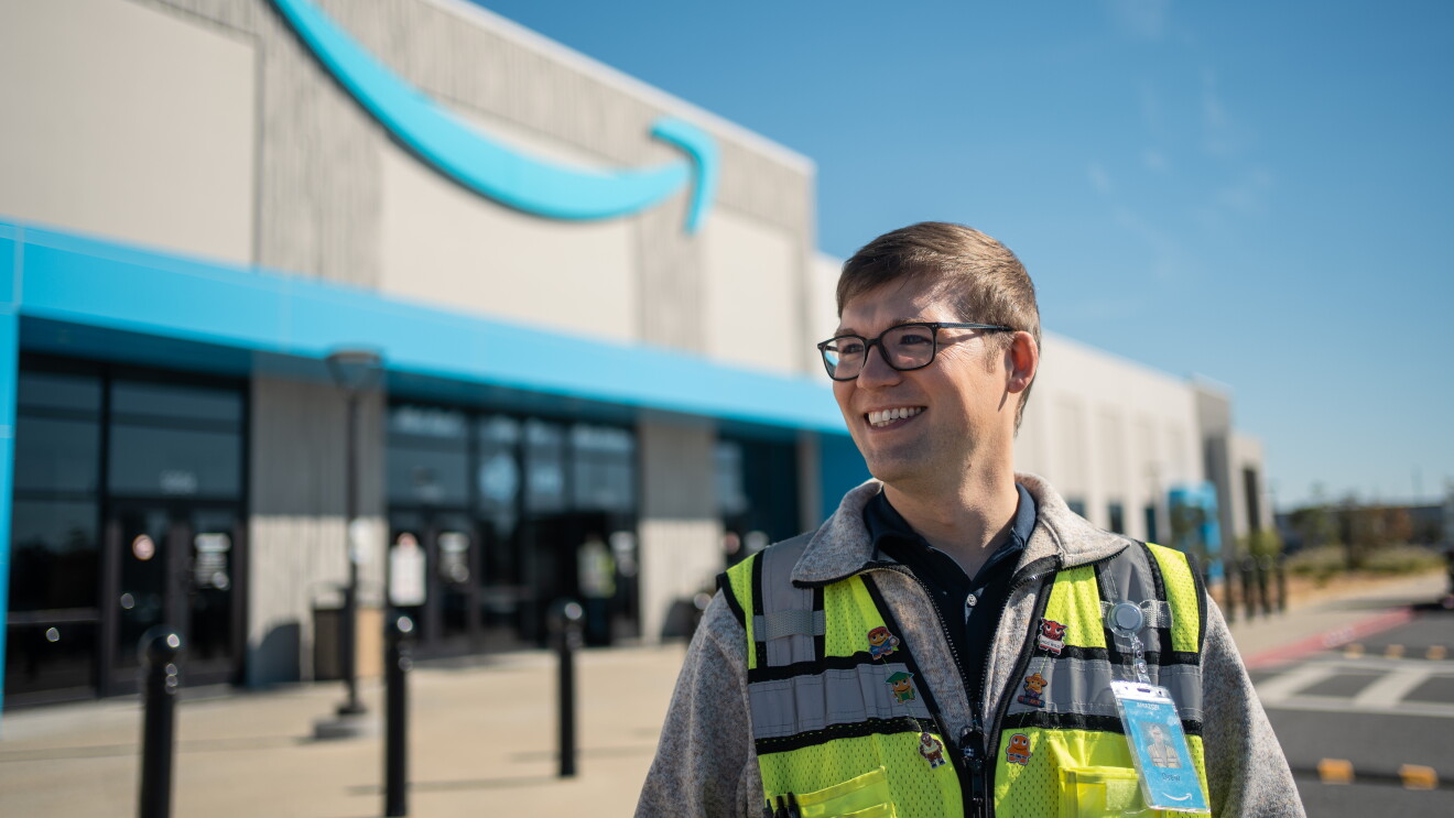 An Amazon employee stands proudly outside of a fulfillment center in a small town. 
