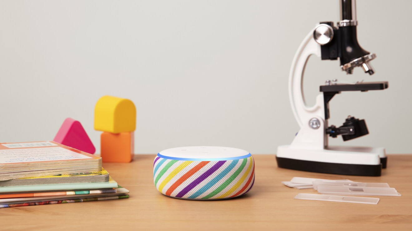 亚马逊在彩虹条纹,回声点显示在一个木制的桌面。左边是书和块,右边是一个显微镜。