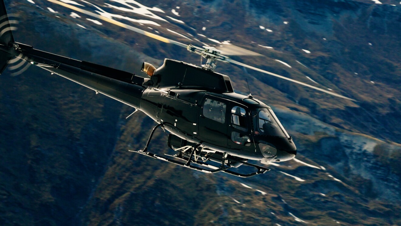 Schwarzer Hubschrauber im Flug über bergigem Gelände