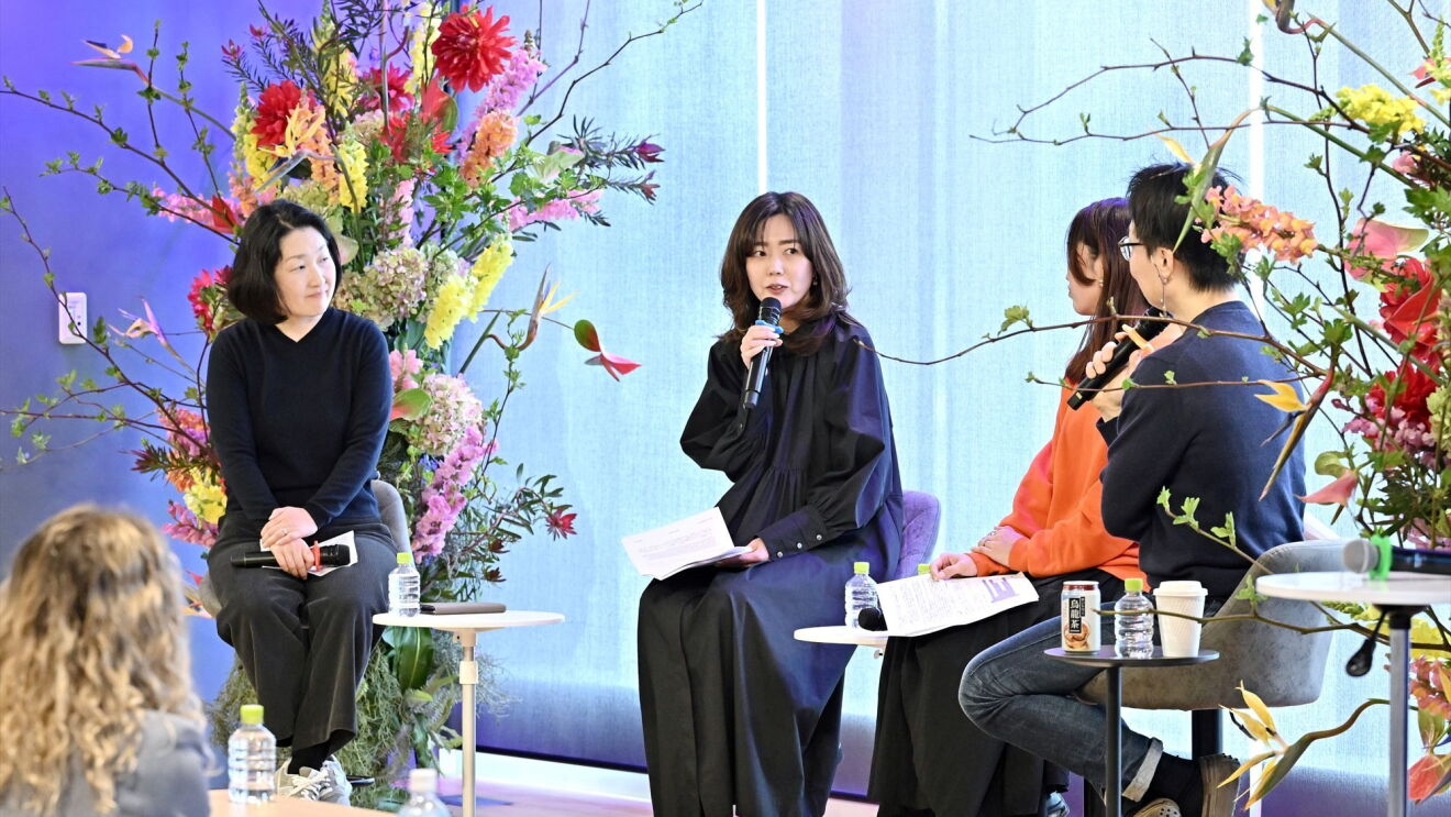 ステージでの話者たちが左から2番目の女性話者の話を聞いている。