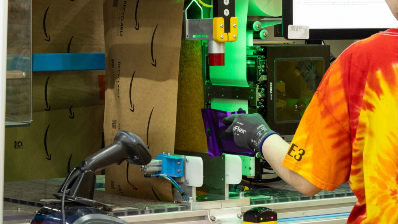 Amazon warehouse worker scanning package with robotic assistance