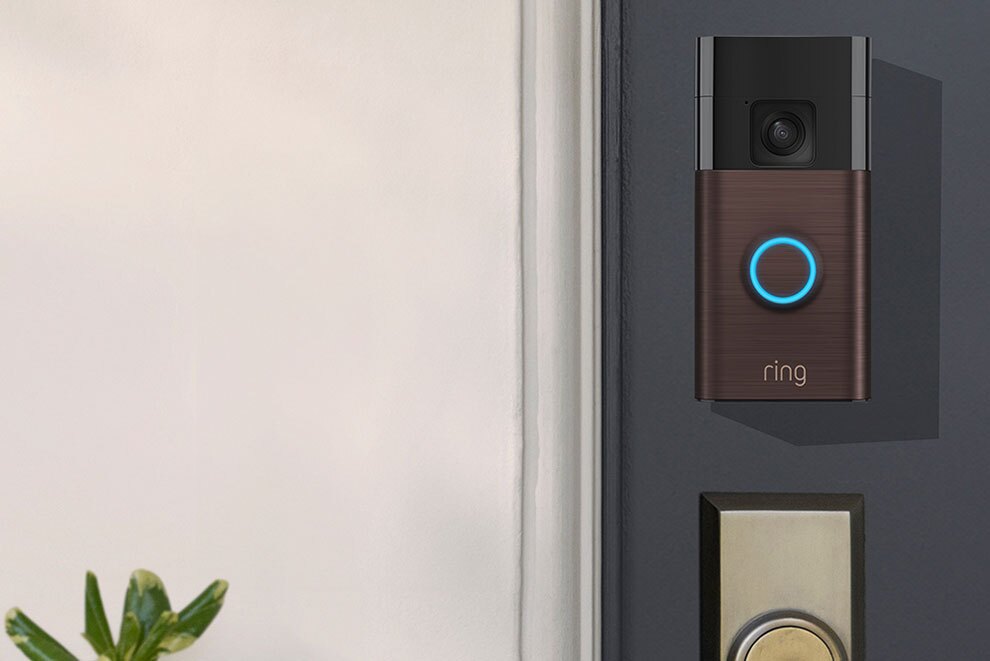 Ringドアベルの本体カラーブロンズが玄関ドアの鍵穴上部に設置され、正面のLEDリングが青く点灯している。