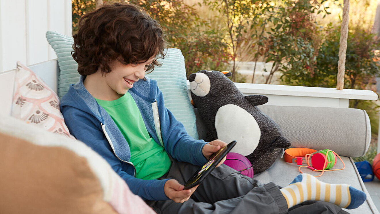 Child sitting on porch, smiling while viewing content on his tablet.