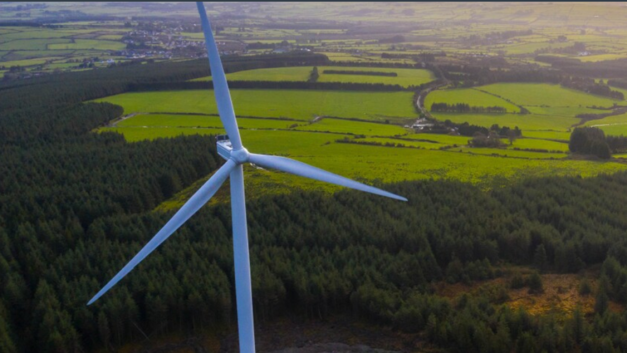 Aerial shot of a wind turbine above green farmlands. 