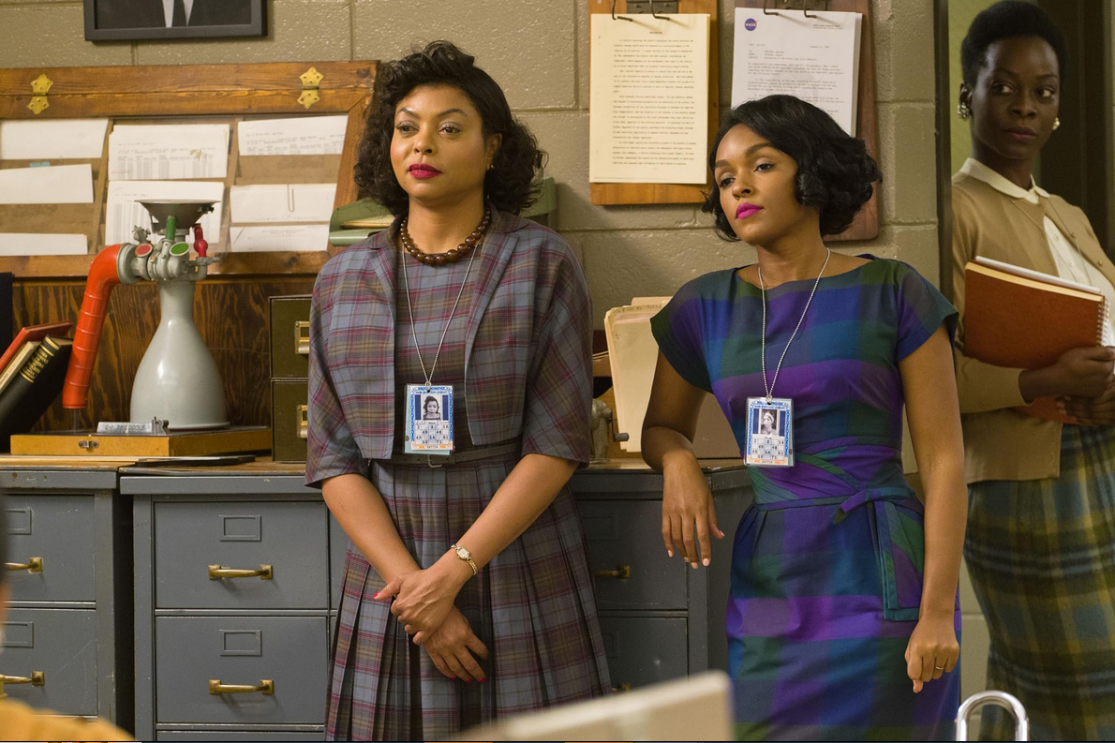 Three women stand by filing cabinets in an office