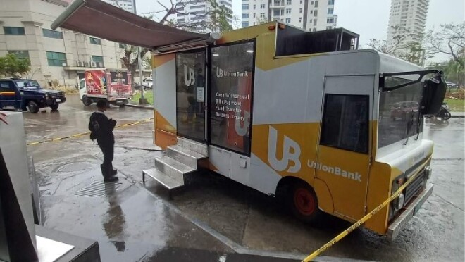 A van with an ATM on board. A lady is standing outside and looking at her mobile phone.