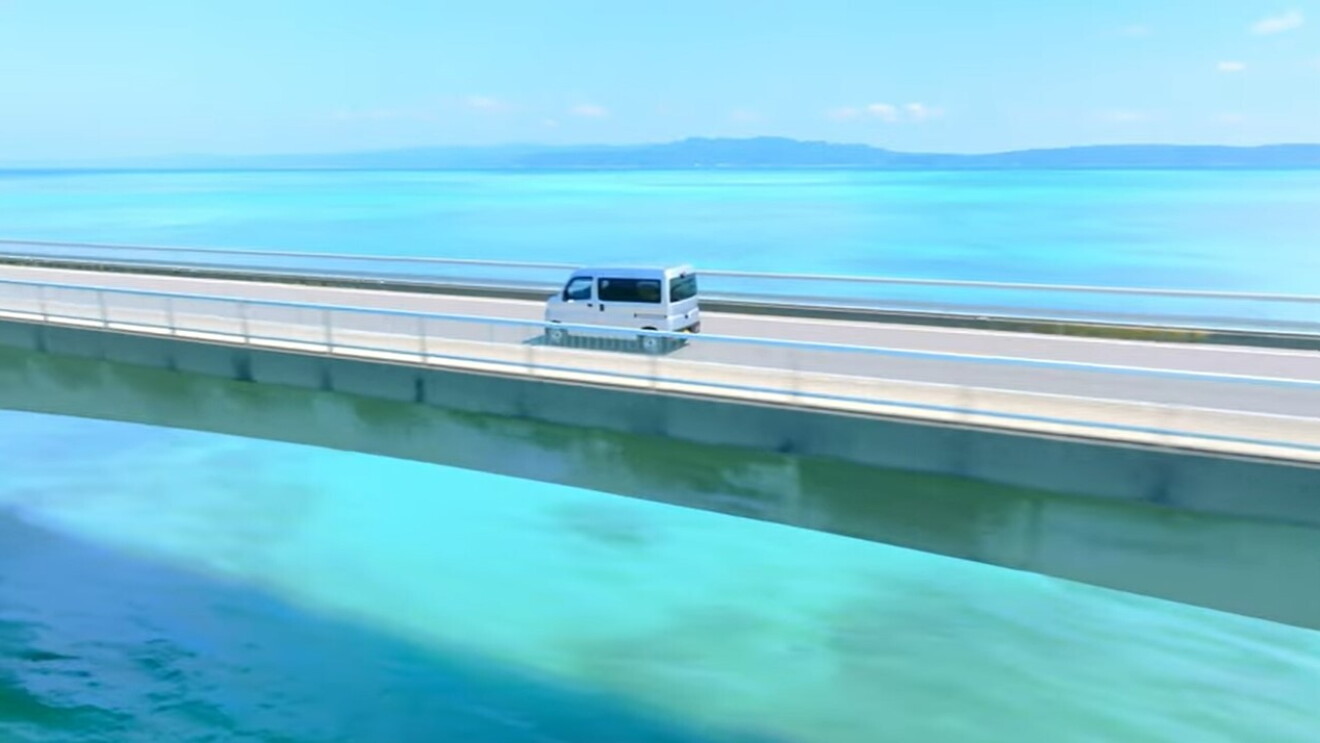 An Amazon delivery vehicle drives across a bridge over very blue ocean water.