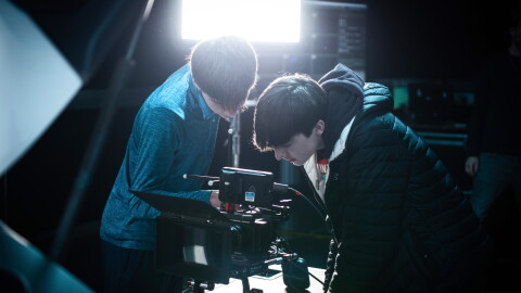 Two people intently examining professional camera equipment on set
