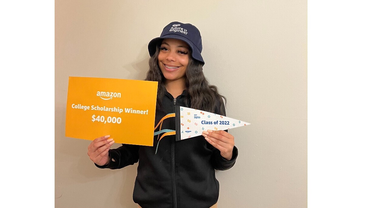 Destiny Ogar smiles and holds up a sign that reads "College Scholarship Winner! $40,000," Ogar also holds a mini flag that reads "Class of 2022."