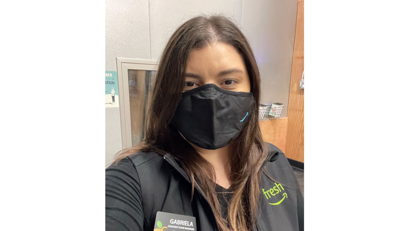 An image of a woman smiling behind a mask for a selfie photo. Her mask has the Amazon logo in the bottom right corner.