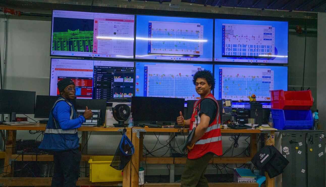 Amazon employees smile in front of several monitoring screens at a Windsor, Connecticut Amazon facility