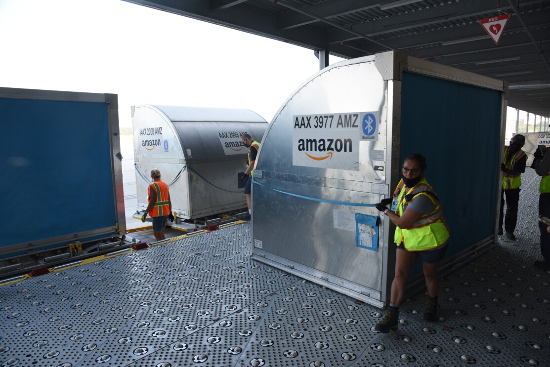 An image of large metal containers being loaded out of the sortation facility through a large door at the loading dock.