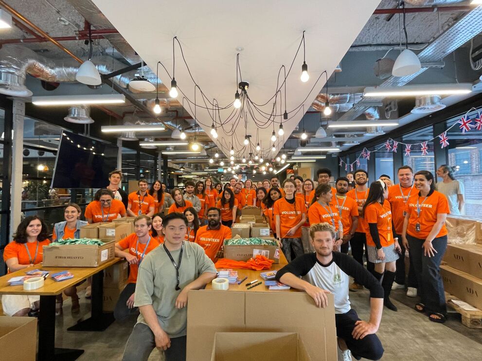 Amazon Mitarbeiter:innen in orangenen T-Shirts in UK stellen Produkte für Spenden zusammen  