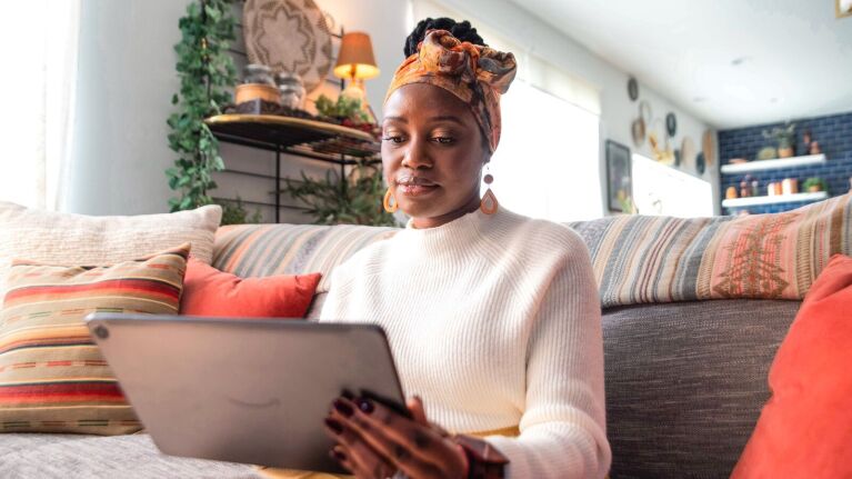 sylvia kapsandoy founder of usimplyspice holds and looks down at a tablet while sitting on a couch