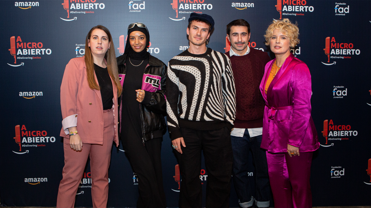 En una imagen de photocall, con el logo de Delivering Smiles y A micro abierto, aparecen: la cómica Carolina Iglesias (con traje chaqueta de color rosa, jersey negro, pelo largo hasta el pecho y una pulsera en la mano derecha), la actriz Hajar Brown (vestida de negro con una chaqueta bomber con una franja rosa fucsia. Lleva gafas de sol encima del pañuelo en la cabeza),  Andrés Ceballos (antiguo vocalista de DVicio vestido con pantalón negro, jersey con estampado de zebra y gorra), el cantante Rayden (vestido con jeans, camisa azul y jersey morado) y  la presentadora Tania Llasera (traje chaqueta rosa fucsia, jersey naranja).