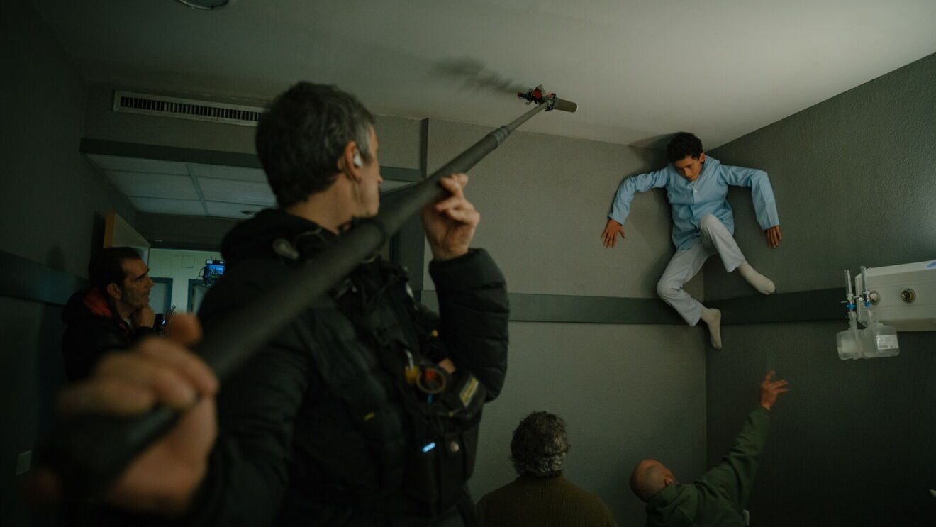 Man holding filming microphone toward a boy in the air on set