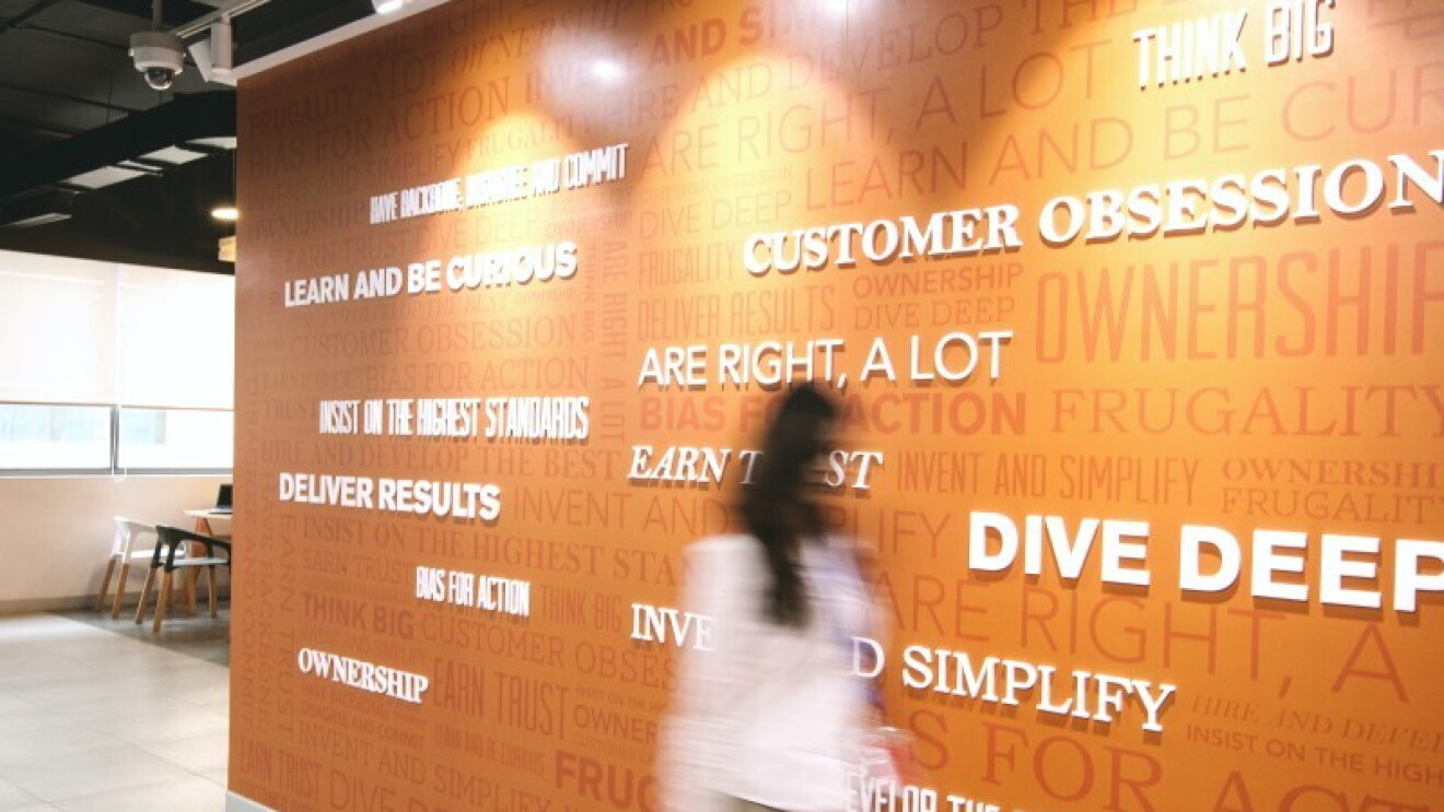 A woman walks past a wall featuring Amazon leadership principles