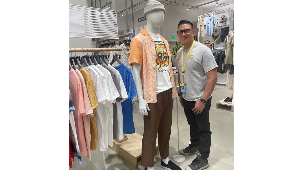 An image of a man standing next to a mannequin dressed in a beanie and a sublime shirt in a store.