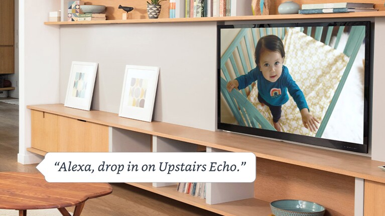 An image of a living room with a TV that shows a kid inside a crib looking at the camera. There is a text box at the bottom that reads "Alexa, drop in on Upstairs Echo."