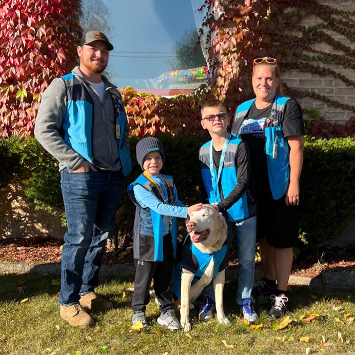 Sawyer poses for a family picture outside with his parents, brother, and dog. All of them are wearing Amazon delivery driver costumes.