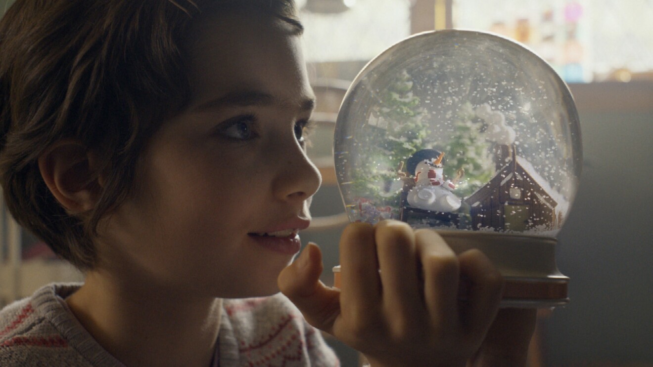 A little girl holds up a snowgloble and stares into it.