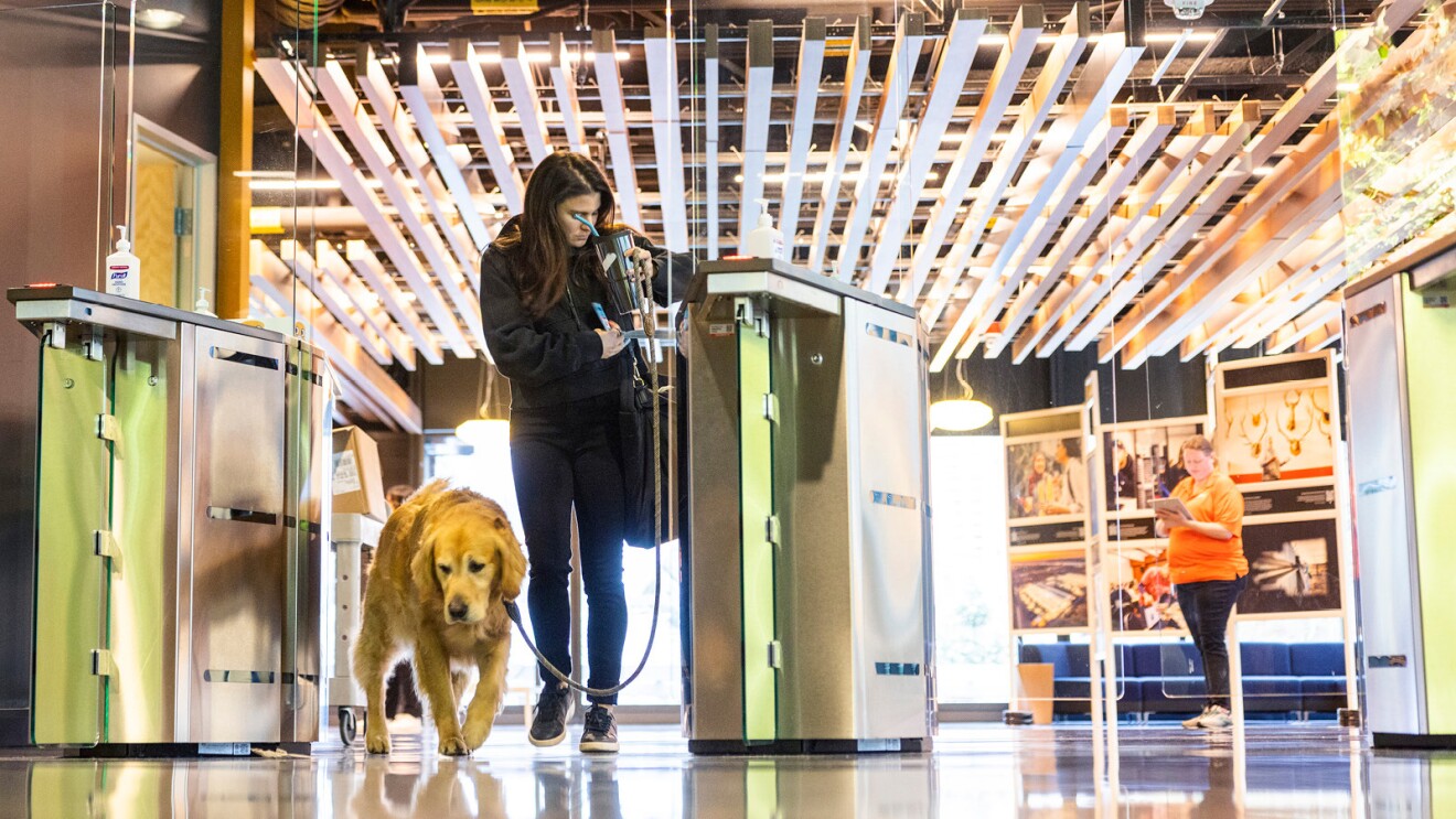 An image of an Amazon employee badging into the Seattle office with a dog next to her on a leash. 