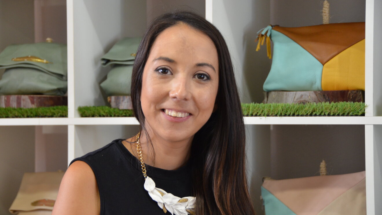 Lilian Urquieta es diseñadora. Posa con pelo largo y vestido negro delante de una estantería llena de los bosos que ella diseña. 

