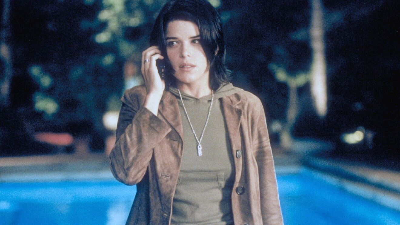 Neve Campbell in brown jacket using cell phone near swimming pool at night in Scream 3