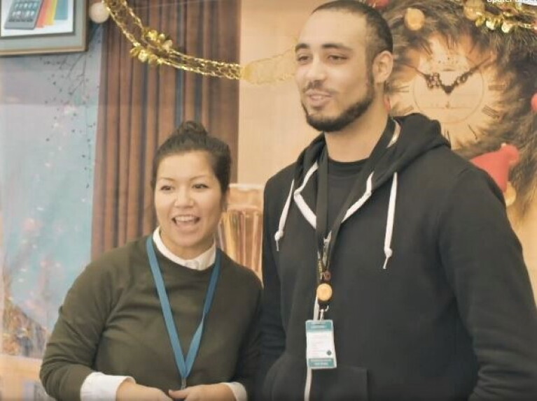 Eine Mitarbeiterin und ein Mitarbeiter: Bei tragen Sweatshirts und sind im Halbkörperprofil zu sehen. Im Hintergrund: Girlanden und weihnachtliche Deko.