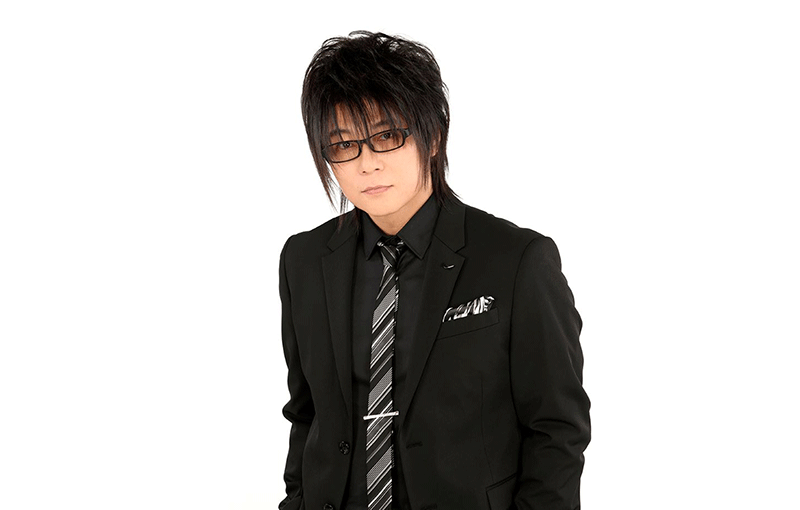 白い背景に、黒いスーツと黒いシャツを着た男性のポートレート。レンズに少し色が入った眼鏡を着用。